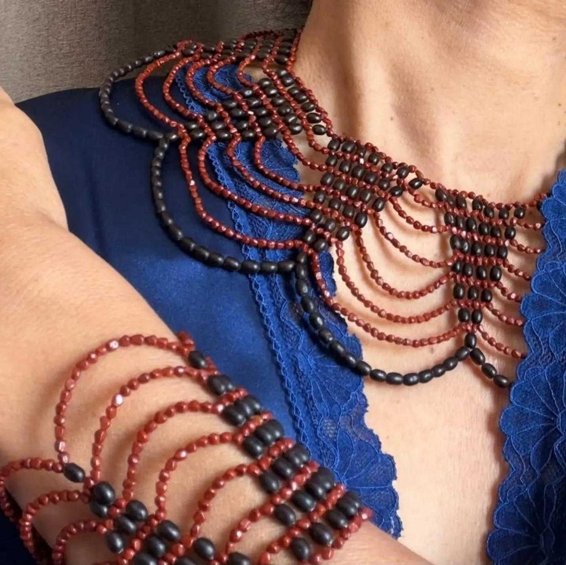 Collar de malla en semillas rojas y negras, con pulsera ancha a juego en la muñeca.